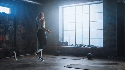 Poster - Fit Athletic Blond Woman Exercises with Jumping Rope in a Loft Style Industrial Gym. She Does Her Intense Cross Fitness Training Program. Facility has Motivational Posters on the Wall.