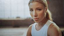 Close-up Portrait Of Beautiful Strong Fit Blond Sitting In A Loft Industrial Gym With Motivational Posters. She's Catching Her Breath After Intense Fitness Training Program. Athlete's Face In Close Up