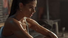 Beautiful Strong Fit Brunette In Sport Top And Shorts In A Loft Industrial Gym With Motivational Posters. She's Catching Her Breath After Intense Fitness Training Workout. Sweat All Over Her Face.