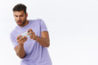 © Cookie Studio - Man focused and excited with awesome new racing game, playing on smartphone, tilt body to move car on mobile phone, looking telephone thrilled and entertained, standing white background