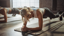 Two Young Fit Atletic Women Hold A Plank Position In Order To Exercise Their Core Strength. They Are Exhausted And Struggling With Training. They Workout In A Loft Gym.