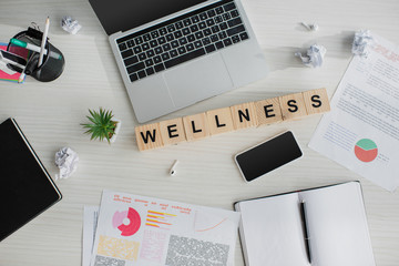 top view of workplace with business documents, laptop, smartphone and alphabet cubes with wellness w