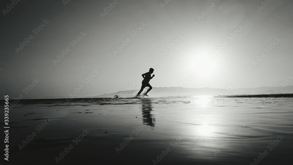 Silhouette Man Running In Water At Beach - obrazy, fototapety, plakaty 