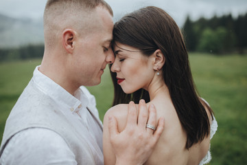 Spring wedding in the mountains. A guy in a shirt and vest and a girl in a white dress hug and kiss on a background of mountains and a forest