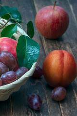 Wall Mural - red grape berries and fresh fruits in a straw basket on a dark wooden background.