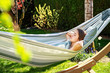 © Tetiana Soares - Young girl relaxing having nap in hammock in garden at home at bright sunny day. Slow living, gadget detox and weekend leisure activity. Quarantine and self isolation period