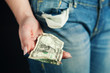 © Liudmyla - Woman with poor manicure pulls out crumpled one-dollar bill from jeans pocket and holds it in her hand. Concept of poverty, economic crisis, coronavirus concept.