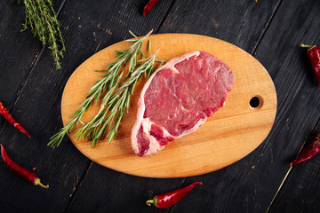 Wall Mural - Top view on piece of fresh raw meat for cooking steak with sprigs of rosemary on a wooden board, horizontal