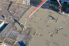Pouring Cement On The Floors Of Residential Multi-story Building Under Construction Using A Concrete Pump Truck With High Boom To Supply The Mixture To The Upper Floors. Aerial High Top Drone View.