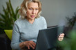 © JENOCHE - Woman lying on a sofa at home concentrating as she works on a laptop