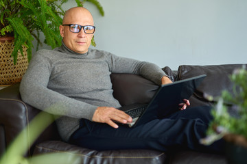 Handsome man wearing glasses and working with notebook while sitting on sofa