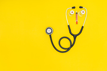 Covid19 vaccine bottles, syringe, needle, and stethoscope on yellow background.Sad face expression using vial, needle, syringe and stethoscope tells healthcare workers working in the covid 19 outbreak