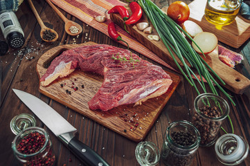 Raw beef rump tail on a cutting board with ingredients and knife