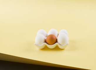 White and one brown egg on light earthy color paper background. Easter, art food creative concept