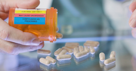 A pharmacist pouring out prescription pills onto a glass table.