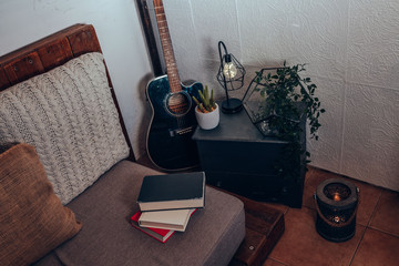 detail of the corner of a comfortable room with guitar, books, cloth stool, plant and a lamp