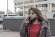 © vladimircaribb - European middle-aged woman hears disturbing news on the phone against the backdrop of modern buildings in the city. Depth of field, background blur