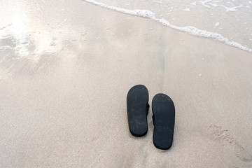 Black slippers on the beach touched by waves from the sea.