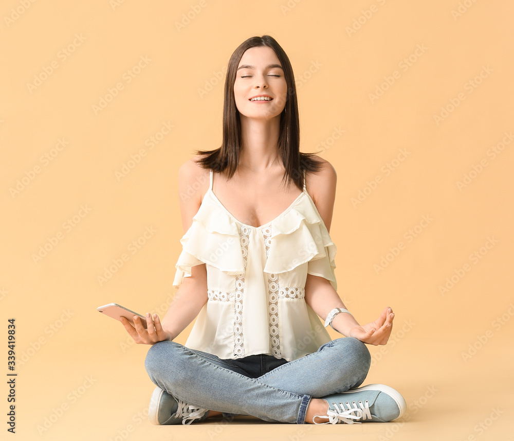 Meditating young woman with mobile phone on color background