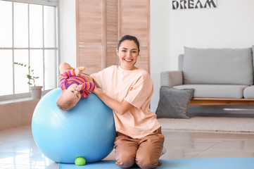 Sticker - Young sporty mother and her baby doing exercises with fitball at home