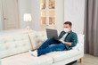 © andrey - freelancer in medical mask working on couch