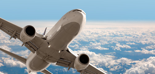 Wall Mural - Passenger airplane flying over snowy mountains - White passenger airplane rising over amazing clouds