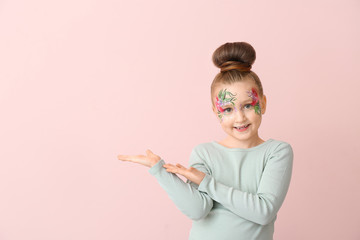 Wall Mural - Funny little girl with face painting showing something on color background