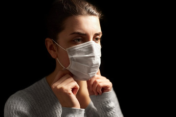 health protection, safety and pandemic concept - sick young woman adjusting protective medical face mask over black background