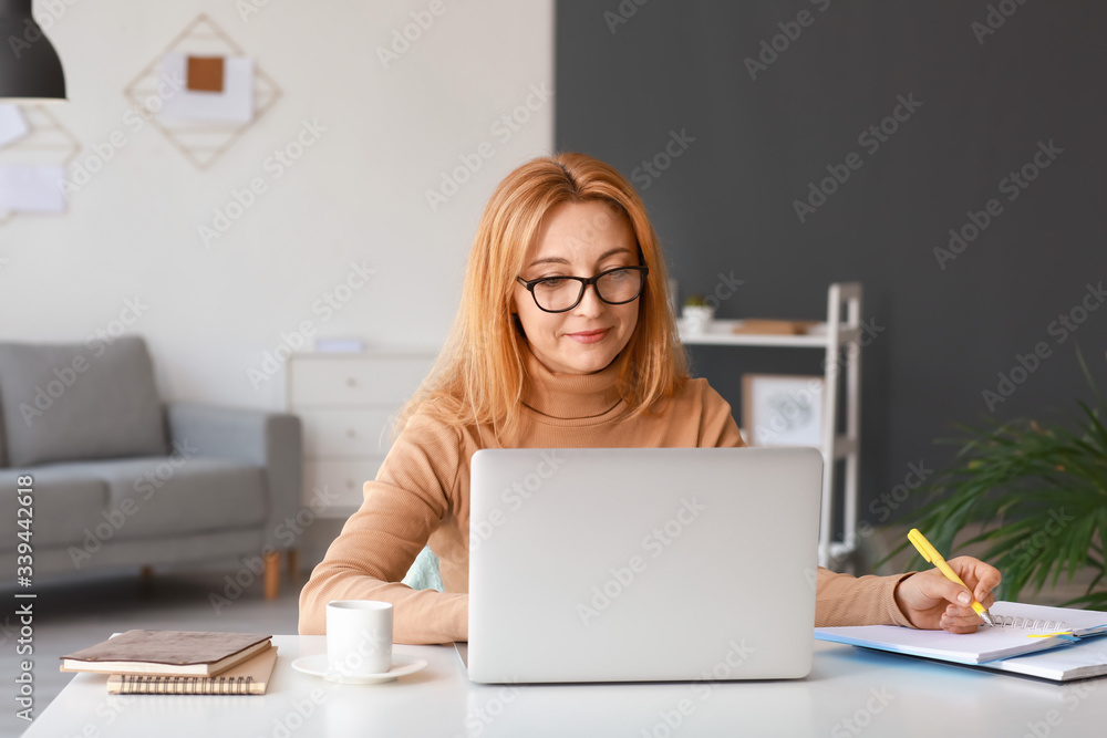 Mature woman using laptop for online learning at home - obrazy, fototapety, plakaty 