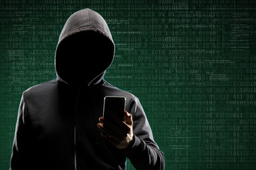 Anonymous computer hacker with a smartphone over abstract digital background. Obscured dark face in mask and hood. Data thief, internet attack, darknet fraud, dangerous viruses and cyber security.