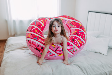 Wall Mural - Summer vacation on quarantine, a kid with donut tube at home, baby girl with pink rubber ring, home self-isolation in summer