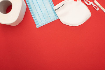 Wall Mural - top view of white toilet paper, safety and medical masks and thermometer on red background