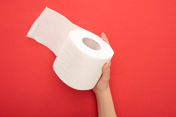 cropped view of woman holding white toilet paper roll on red background