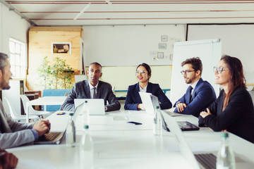 Wall Mural - Group of smiling analysts communicating during meeting. Cheerful young business people talking during briefing. Business meeting concept