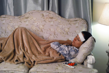 Sick woman sleeping on the couch during a winter night.