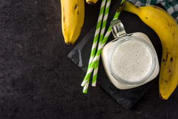 Wall Mural - Banana smoothie in jar on black slate background. Top view. Copy space