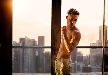 Portrait of sexy shirtless man covered with shadow stripes from window, looking at camera