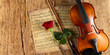 © stockphoto-graf - classic retro violin music string instrumt on old music note sheet paper with red rose flower old oak wood wooden panorama copy space background. classical musical romantic valentines day concept.
