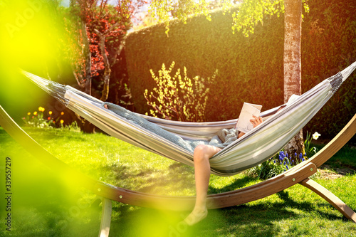 Young relaxed girl reading book in hammock in garden at home at bright sunset Tableau sur Toile