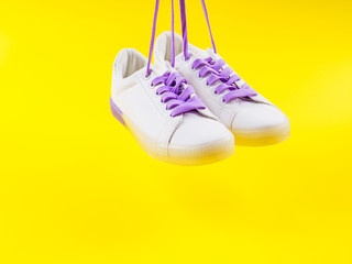 Wall Mural - White sneakers with purple laces on yellow background. Modern minimal fashion art trendy bold color still life