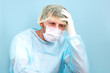 © alenaphoto - Tired doctor scientist in lab coat, surgical cap and mask sits and takes break.