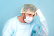 © alenaphoto - Tired doctor scientist in lab coat, surgical cap and mask sits and takes break.