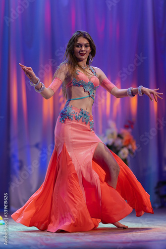 Dancer with long hair in orange neon  oriental costumes dance belly dance on the concert stage