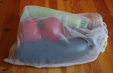 Vegetables packed in a reusable mesh bag on wooden background. Eco-friendly packaging. Close-up. Indoors.