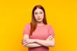 © luismolinero - Young redhead woman over isolated yellow background keeping arms crossed