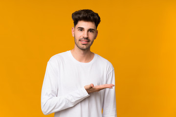 Wall Mural - Young man over isolated orange background presenting an idea while looking smiling towards