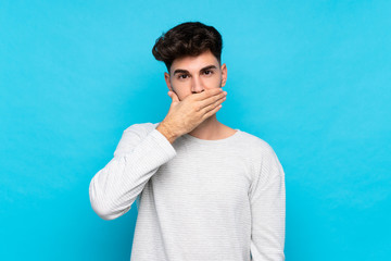 Wall Mural - Young man over isolated blue background covering mouth with hands