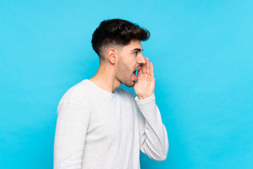 Wall Mural - Young man over isolated blue background shouting with mouth wide open to the lateral