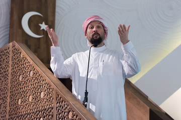 Wall Mural - Muslims young arabic Imam has a speech on friday afternoon prayer in mosque. Muslims have gathered for the friday afternoon prayer in mosque and are listening to the speech of imam