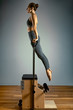 © Georgii - Young girl exercises on a bed of Pilates reformers, in the hall on a background of a gray wall. Fitness stretching concept. Healthy body, yoga, Pilates, copy space